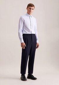 Jasnoniebieska koszula na guziki z bawełny, zestawiona z ciemnogranatowymi plisowanymi spodniami i czarnymi eleganckimi butami, o jednolitej, gładkiej fakturze.