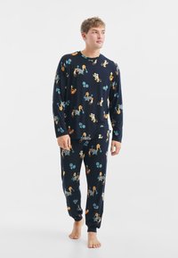Conjunto de pijama en color navy que incluye mangas largas y pantalones, decorado con coloridos leones de dibujos animados y elementos deportivos, hecho de una tela suave con un ajuste relajado.