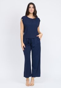 Top blu navy con dettagli in bottoni dorati sulle spalle, abbinato a pantaloni a gamba larga coordinati, caratterizzati da una vestibilità morbida e vita con cordoncino.