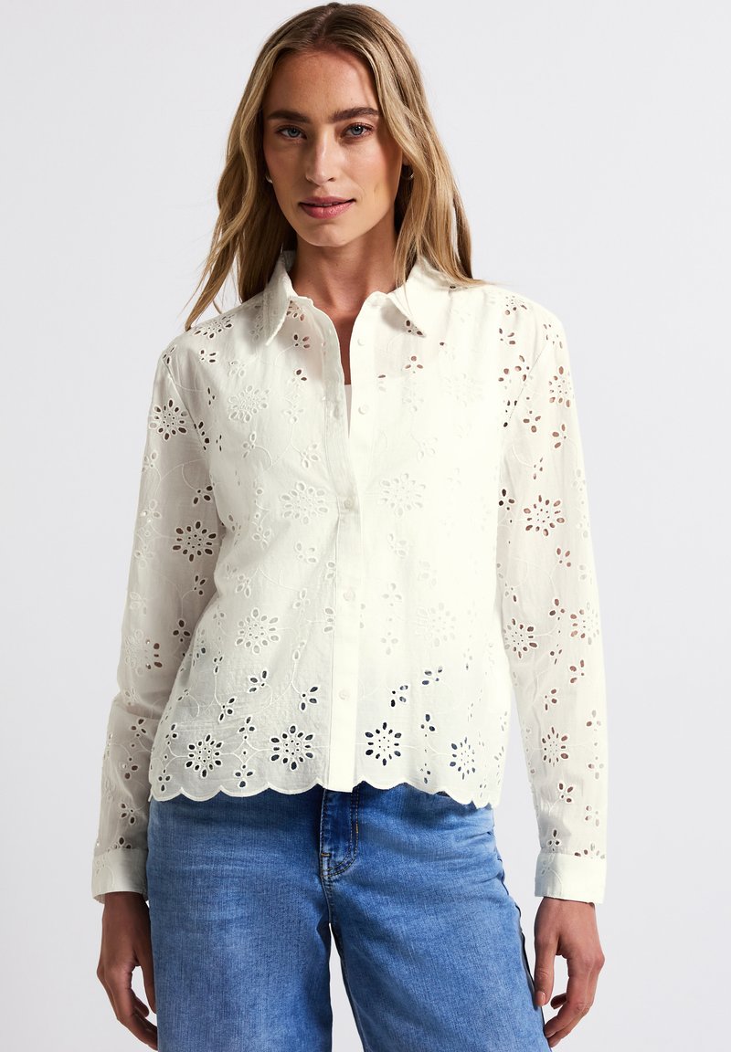 Vit bomulls skjorta med vågig nederkant, med blommig urklippade mönster, långa ärmar och knäppning fram. Bärs med blå jeans.