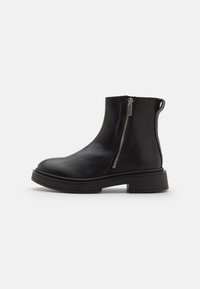 Botine din piele neagră, cu fermoar pe lateral, vârf rotund și talpă groasă neagră. Textură netedă și design modern, cu loop de prindere.