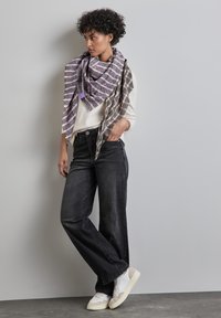 Écharpe grise et violette à motifs drapée sur un pull crème, associée à un jean noir ample et des baskets blanches avec des accents beiges.