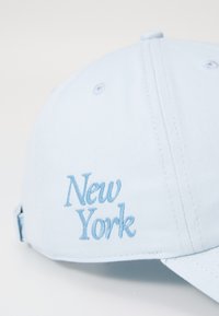 Hele sinine pesapallikeep, millel on tikitud "New York" sama tooni sinisega. Valmistatud siledast kangast, tagaküljel reguleeritav rihm.