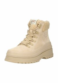 Beige suède enkellaars met een zachte fleece kraag, ronde neus en dikke rubberen zool. Voorzien van een vetersluiting en metalen oogjes.