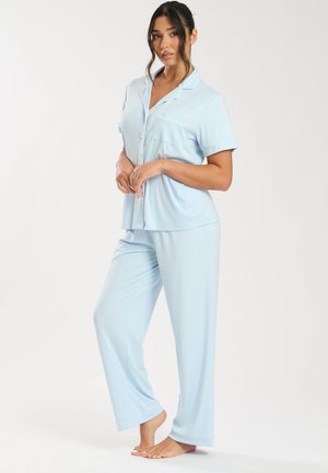Ensemble de pyjama bleu clair comprenant un haut à manches courtes avec boutons et une poche, ainsi que des pantalons longs, fabriqué dans un tissu doux et lisse.
