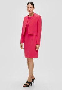 Blazer rose et robe assortie, toutes deux en tissu élégant. Le blazer présente un design court, assorti à des sandales noires à talons hauts.