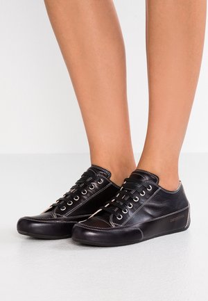 Voeten met zwarte leren veterschoenen met witte stiksels op een gladde lichtgrijze vloer.