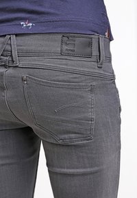 Grå denimjeans med rak passform, med en läderpatch, kontrasterande sömmar och två bakfickor med subtila detaljer.