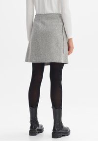 Grauer Tweed-Rock mit figurbetonter Silhouette, Seitentaschen-Detail und einem Saum, der oberhalb des Knies endet. Kombiniert mit schwarzen Stiefeletten und Strumpfhosen.