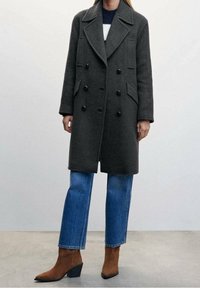 Donkergrijze dubbelzijdige jas van wolmix, met grote zwarte knopen en twee voorzakken, gecombineerd met blauwe rechttoe-rechtaan jeans.