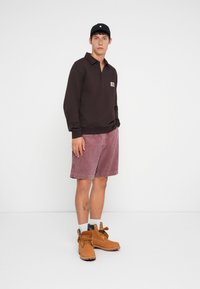 Brown long-sleeve polo shirt with a logo, pink shorts, and tan work boots with black laces. Plain background with no additional details.