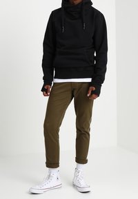 Felpa nera con cappuccio e collo a scialle, abbinata a pantaloni verde oliva a coste strette e sneakers alte bianche. Casual, vestibilità comoda.