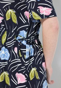 Kwiatowa sukienka wykonana z ciemnonawowej tkaniny z różowymi, niebieskimi i zielonymi wzorami kwiatów, z dopasowanym sznurkiem w talii.