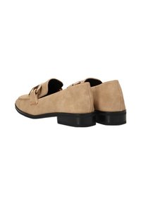 Mocasines de ante beige con una textura suave, punta redondeada y un bajo tacón negro. Presentan detalles de costura y una hebilla decorativa en la parte frontal.