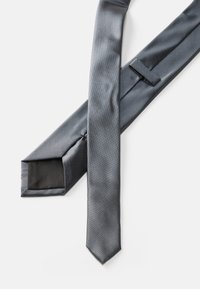 Corbata de seda gris con una textura suave, que presenta un extremo puntiagudo y un lazo para asegurar. Brillo sutil y color sólido sin patrones.