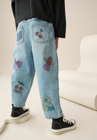 Lysblå denim jeans med forskellige farverige applikationer, herunder blomster, kirsebær og hjerter, i en afslappet pasform.