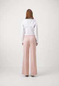 Witte cropped shirt met gedetailleerde achternaad, gecombineerd met hooggehakte, brede pastelroze broeken en zwarte hakken.