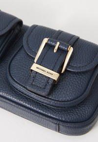 Geantă din piele texturată de culoare bleumarin, cu o cataramă aurie și o placă pe închidere cu inscripția "MICHAEL KORS".