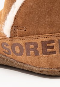 Braune Wildlederstiefel mit einem weichen weißen Fleece-Futter und eingeprägtem Logo. Obermaterial an der Naht genäht mit einer strapazierfähigen, strukturierten Sohle.