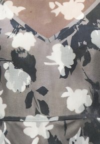 Μπεζ και γκρι ύφασμα με ασπρόμαυρο λουλουδένιο σχέδιο και διακριτική ραφή σε σχήμα V.