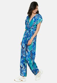 Žydros ir žalios gėlėmis margintas šokinėjantis kostiumas su trumpomis rankovėmis, V formos iškirpte ir surišta juosmens dalimi. Dėvima su baltomis sportinėmis avalynėmis.