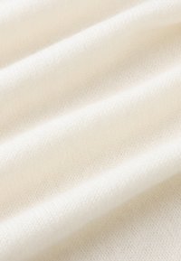 Tessuto morbido e texturizzato di colore bianco sporco con una superficie liscia e un sottile motivo a costine, che mette in mostra delicati pieghe e strati.