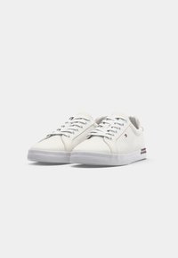 Valged kangast sneakers, madala disainiga, hallide paeltega, kummist tallaga ja külgedel punase ja sinise triibuga aktsentidega.