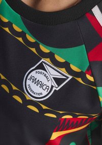 Logo der Football Federation von Jamaika auf einem Sporttrikot mit Muster in Schwarz, Grün, Gelb und Rot und einem schwarzen Kragen.
