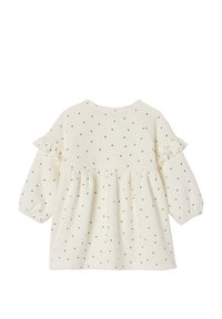 Cremefarbenes Kleid mit langen Ärmeln, Rüschendetails und gerafftem Bund, das ein durchgehendes schwarzes Punkte Muster aufweist.