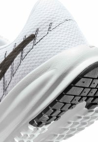 Chaussure de sport blanche avec une tige en mesh texturé, des accents noirs et une semelle en caoutchouc avec un motif de semelle pour l'adhérence et le soutien.