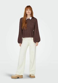 Brun stickad tröja med V-hals och puffärmar, kombinerad med vita vida jeans och beige plattformsskor. Vit skjorta med krage under.