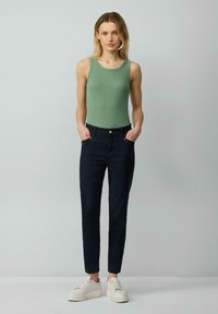 Pantalons bleu marine foncé à coupe ajustée, associés à un débardeur côtelé vert clair et des baskets blanches, avec un design simple et des détails minimaux.