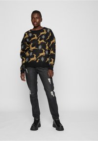 Pull noir avec motif de cerf doré et flocons de neige blancs. Associé à un jean noir usé et des bottes noires robustes. Design simple et décontracté.