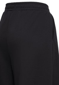 Pantalon noir à taille élastique avec poches latérales et tissu lisse légèrement texturé en gros plan.
