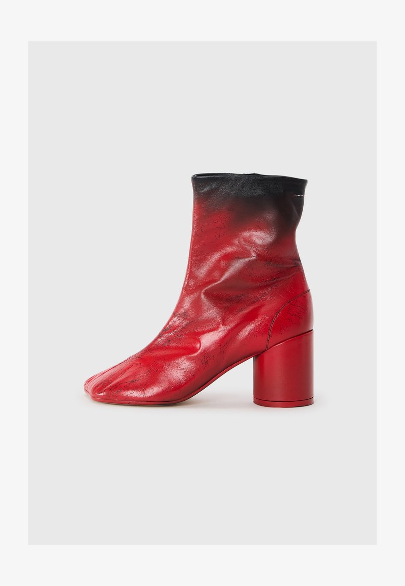 Czerwony skórzany botek za kostkę o teksturowanym wykończeniu, z czarnym mankietem i masywnym czerwonym obcasem. Posiada unikalny, spiczasty czubek.