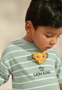 Roheline triibuline puuvillane T-särk, millel on kollane Simba graafika ja mustalt broderitud "Disney KUNINGAS LÕVI" tekst.
