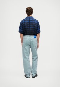 Cămașă cu mânecă scurtă, cu un model în carouri albastre, asortată cu blugi albaștri deschiși. Cămă�șa are un guler clasic și un logo pe spate.