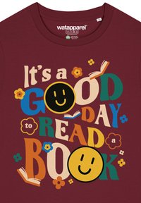 T-shirt bordeaux avec un texte multicolore : « C'est une BONNE journée pour LIRE un LIVRE » avec des icônes de visages souriants et des accents floraux.