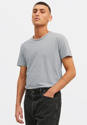 Helles graues Baumwoll-T-Shirt mit Rundhalsausschnitt und kurzen Ärmeln, kombiniert mit schwarzen Jeans aus Denim, die einen lockeren Schnitt und ein minimalistisches Design aufweisen.