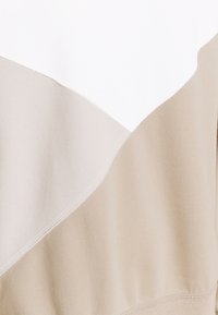 Sudadera color bloque en tonos beige y blanco con una textura suave. Presenta un diseño diagonal y puños acanalados, con detalles de costura visibles.