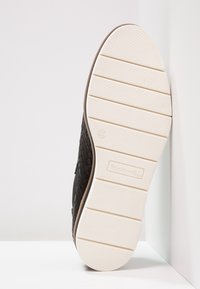 Zapato de tela tejido negro con suela de goma blanca, con un patrón texturizado y un diseño de puntera redondeada. Talla 37 marcada en la suela.