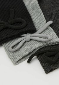 Tre articoli in maglia di colore nero, grigio e grigio scuro. Ognuno presenta una texture a coste e nastri di tessuto nei colori corrispondenti.