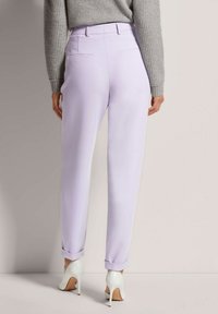 Lavender tailored trousers with a smooth texture, featuring a rolled hem, dual back pockets, styled with white high-heeled shoes.
