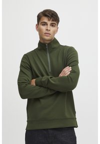 Grön zip-up hoodie med hög krage, tillverkad av ett mjukt tyg, med en strukturerad passform och ribbade ärmslut och nederkant.
