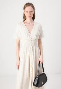 Abito beige a lunghezza ginocchio, con scollatura a v, maniche corte e vita arricciata, caratterizzato da dettagli con bottoni sul davanti e sottili righe.