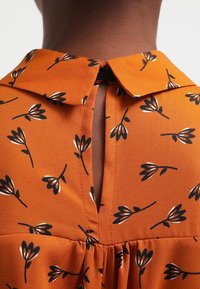 Abito arancione con motivo floreale, colletto e dettaglio a chiave sul retro, caratterizzato da una texture morbida e liscia e vita arricciata.