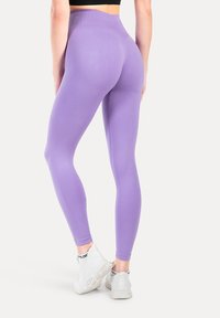 Leggings morados de tiro alto con una textura suave y un diseño ajustado. Llevados con zapatillas deportivas blancas, mostrando un estilo minimalista.