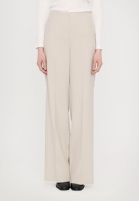 Beige wijde broek gemaakt van gladde stof, met een hoge taille en een strak design, gecombineerd met eenvoudige zwarte schoenen.