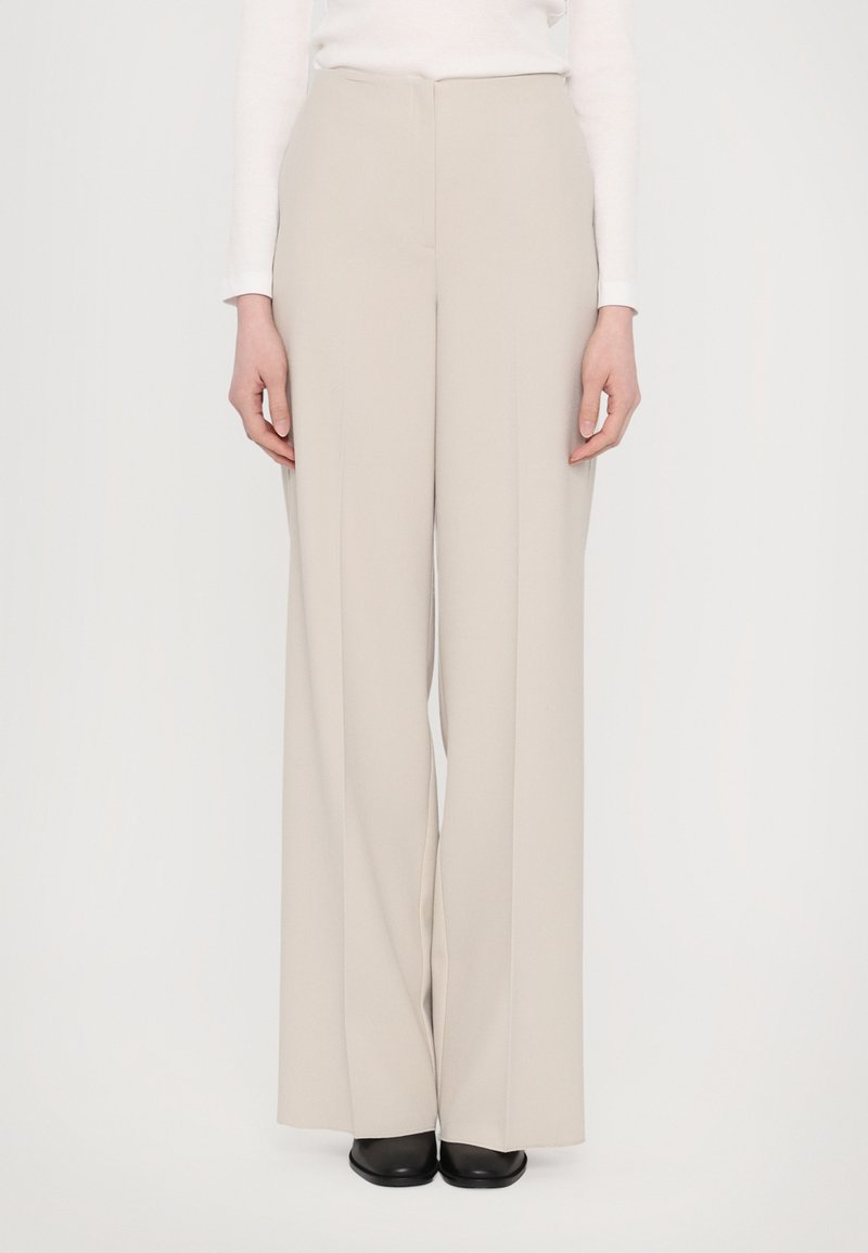 Beige wijde broek gemaakt van gladde stof, met een hoge taille en een strak design, gecombineerd met eenvoudige zwarte schoenen.