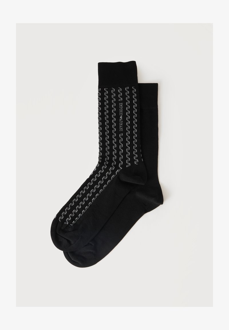 Paire de chaussettes noires mi-mollet, dont une présente des bandes réfléchissantes verticales en zigzag et le texte "Emporio Armani" sur un fond uni clair.